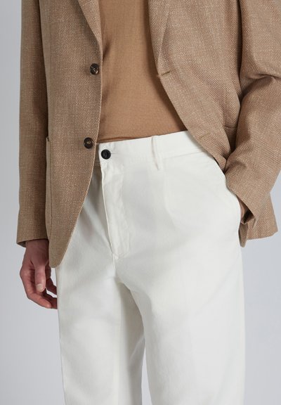 Blazer texturizado en color beige, combinado con una blusa beige y pantalones blancos. Los pantalones tienen un cierre de botón y un acabado de algodón suave.