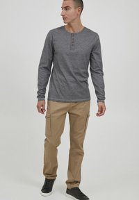 Grå langermet skjorte med rund hals og tre brune knapper, kombinert med beige cargo-bukser med sidelommer og svarte joggesko.