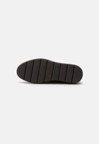 Schwarze Gummisohle mit horizontalen Rillen, einer strukturierten Oberfläche und einem rechteckigen Logodetail in der Mitte.