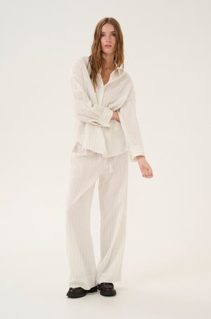 White, lightweight striped shirt and matching loose pants, featuring subtle vertical lines and long sleeves. Black shoes complete the outfit.