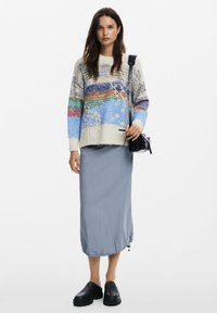 Kötött pulóver színes csíkokkal és texturált mintával; egy világoskék midi szoknyával és fekete platform cipőkkel párosítva. Fekete crossbody táska.