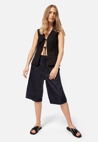 Top senza maniche nero con lacci frontali, abbinato a culotte in denim scuro e sandali neri flat. Tessuto morbido con una vestibilità rilassata.