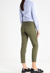 Olivgröna figursydda byxor med midjehöjd och avsmalnande ben. I kombination med en ljusblå skjorta med knappar och svarta loafers.