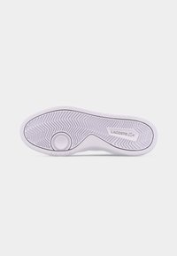 Hvit såle fra Lacoste-sneakers som viser detaljert mønster og logo på en ensfarget hvit bakgrunn.