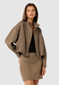 Brun og tan ternet cropped jakke med udtalte skuldre, høj krave og knaplukning, parret med en matchende mini nederdel.