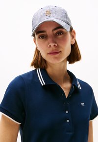 Navy polo shirt with white stripe accents on collar and sleeves, matched with a blue and white striped cap featuring a gold logo detail.