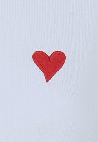 Valge sokk, millel on punane tikandiga südame disain. Süda on keskendatud ja silmatorkav oma sujuva, tekstuuriga õmbluse poolest kanga vastas.