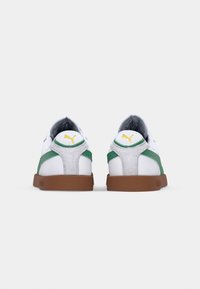 Sneakers bianche con accenti verdi e pelle scamosciata grigia sul tallone. Suola in gomma marrone, con un logo giallo sul retro.