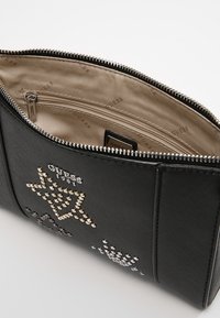 Svart faux läder clutchväska med rhinestone-accenter, dragkedjestängning och en beige tyginteriör som har en dragkedjeficka och varumärkeslogotyp.