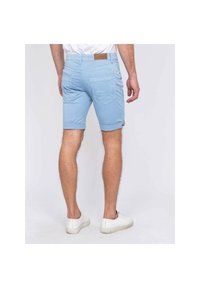 Shorts en coton bleu clair avec ourlets roulés, deux poches arrière et une étiquette en cuir beige sur la ceinture. Portés avec des baskets blanches.