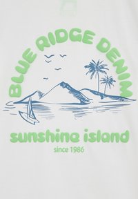 Balta medvilnės marškinėliai su mėlynais piešiniais, vaizduojančiais kalnus, jachtą ir palmės, su žaliais užrašais: "BLUE RIDGE DENIM" ir "saulės sala nuo 1986 metų."