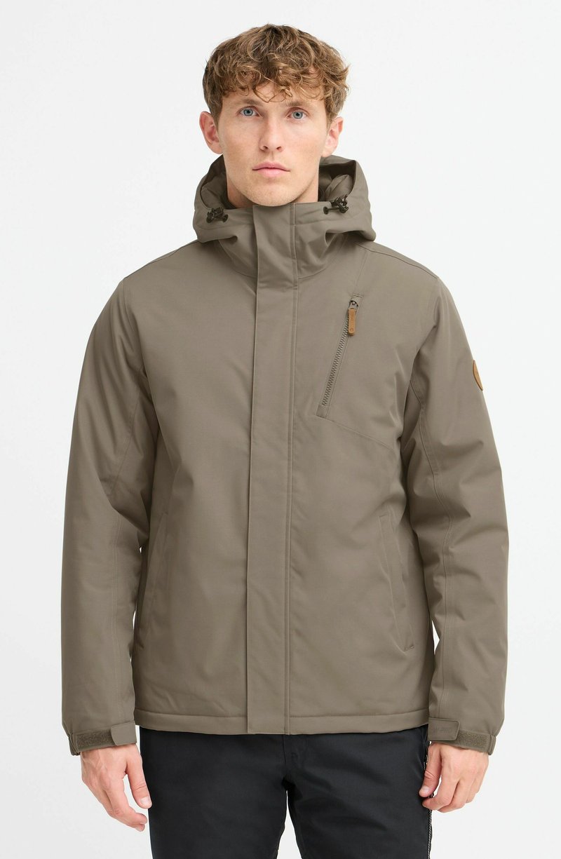 Chaqueta impermeable marrón con un alto cuello y capucha ajustable, que cuenta con un bolsillo con cremallera en el pecho y un parche con el logotipo en la manga izquierda.