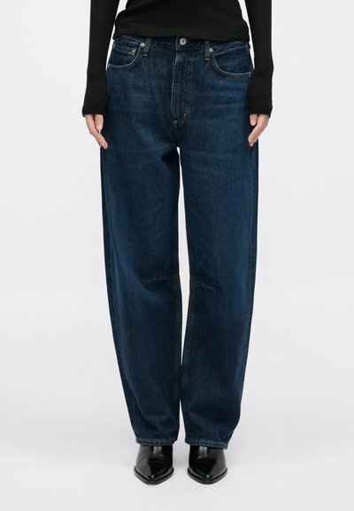 Sötétkék, laza szabású farmernadrág öt zsebbel, gombos záródással és kontrasztos varrással. Sima tapintású anyag.