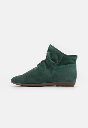 Bottine en daim vert foncé avec une tige légèrement froissée et une semelle plate marron, vue de profil sur fond blanc.