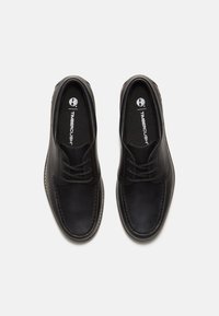 Zapatos de cuero negro con un acabado suave, punta redonda, diseño de cordones y costuras visibles a lo largo de la suela. Cuenta con una plantilla acolchada.