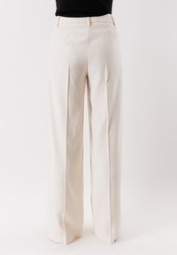 Pantaloni beige a vita alta con design a gamba larga, caratterizzati da pieghe frontali e una texture liscia, adatti per abbigliamento formale o casual.