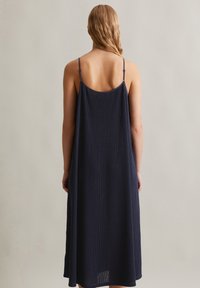 Navy Kleid mit dünnen verstellbaren Trägern, lockerem Schnitt und gerippter Textur. Knie-lange Länge mit leichter A-Linie und minimalistischem Design.