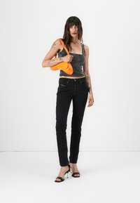 Black skinny jeans, fitted black and white polka dot tank top, and a bright orange handbag. Model wearing black high-heeled sandals.