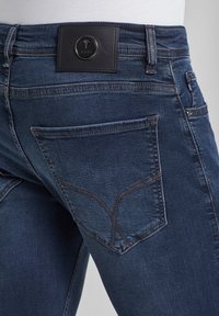 Mörkblå denimjeans med läderpatch med logotyp och detaljstickning på bakfickorna, slim-fit design och standard midja.