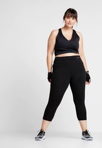 Svart atletisk crop-top og høytlivs tights laget av elastisk stoff med en jevn tekstur. Kommer med svarte treningshansker og joggesko.