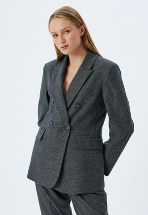 Blazer doppiopetto grigio a scacchi houndstooth con rever a punta, due bottoni e vestibilità rilassata. Tessuto testurizzato con due tasche frontali.