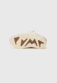 Kremfargede sneakers med en teksturert gummisåle. Har et hevet brunt akssent og bølgemønstre på yttersålen for bedre grep.