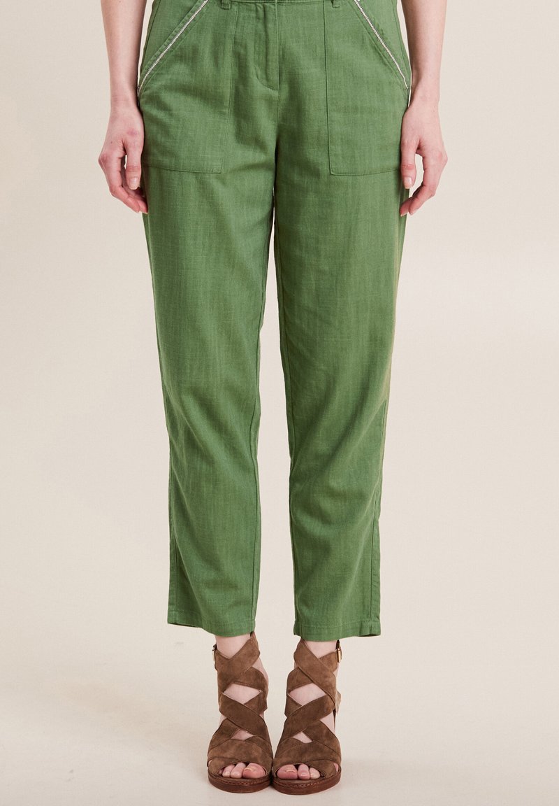 Groene linnen broek met zijzakken, voorzien van witte stiksels. Gecombineerd met bruine suède sandalen met bandjes. Perfecte pasvorm.