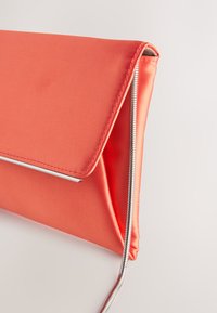 Pochette en satin corail avec fermeture à rabat, quincaillerie de ton argent et détail zippé sur le côté. Texture lisse, design structuré.