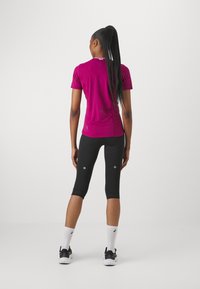 Top sportivo magenta attillato a maniche corte in tessuto testurizzato, abbinato a leggings neri a tre quarti con dettagli riflettenti e taglio alla caviglia.