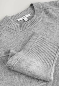 Zacht grijs gebreid sweater met geribbelde ronde hals en manchetten, gelabeld "Next," plat neergelegd op een neutrale achtergrond.
