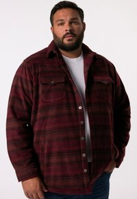 Rød og sort ternet flannel skjorte med spidse kraver, to brystlommer og knaplukning foran, båret over en hvid t-shirt.