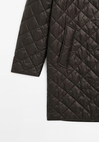 Mørkebrun quiltet frakkeærme og -side med diagonal diamantstikning og en rektangulær sidelomme på en hvid baggrund.