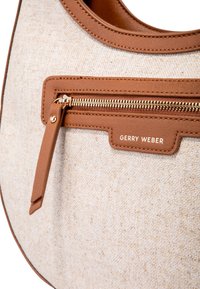 Borsa tote realizzata in un tessuto beige chiaro texturizzato, con dettagli in pelle marrone, tasca con zip dorata e logo, progettata per la funzionalità.