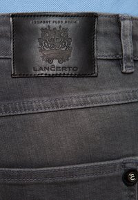 Szare dżinsy z denimu z teksturowaną czarną skórzaną metką z wytłoczonym herbem i logo. Ciekawe detale przeszycia wzdłuż kieszeni.