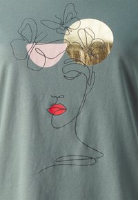 T-shirt en coton vert avec un design abstrait représentant le visage d'une femme, des lèvres rouges et des accents floraux dorés et roses.