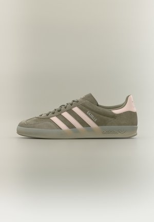 Adidas Gazelle Sneaker aus olivgrünem Wildleder mit blassrosa Streifen, Fersenlasche und durchsichtigem Absatz, seitlich auf neutralem Hintergrund dargestellt.