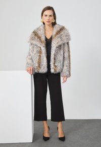 Chaqueta de pelaje sintético con manchas de leopardo en gris y marrón, cuello oversized y mangas largas, combinada con pantalones de pierna ancha negros y tacones.