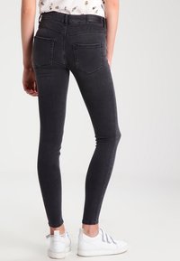 Jeans negros ajustados de talle alto, con bolsillos delanteros y traseros, y una textura suave, combinados con zapatillas blancas.
