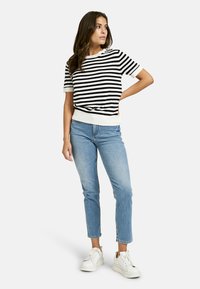 Black and white striped short-sleeve sweater with a ribbed hem, paired with light blue jeans and white sneakers. Minimalist design.