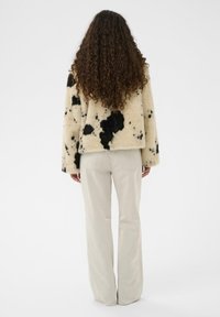 Jakna iz umetnega krzna v krem barvi s črnim pikastim vzorcem, z dolgimi rokavi in širokim krojem; kombinirana z bež širokimi hlačami.