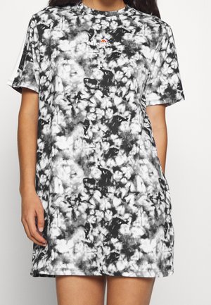 Kobieta nosząca czarno-białą sukienkę T-shirt z krótkim rękawem w stylu tie-dye z małym, kolorowym logo Ellesse na piersi.