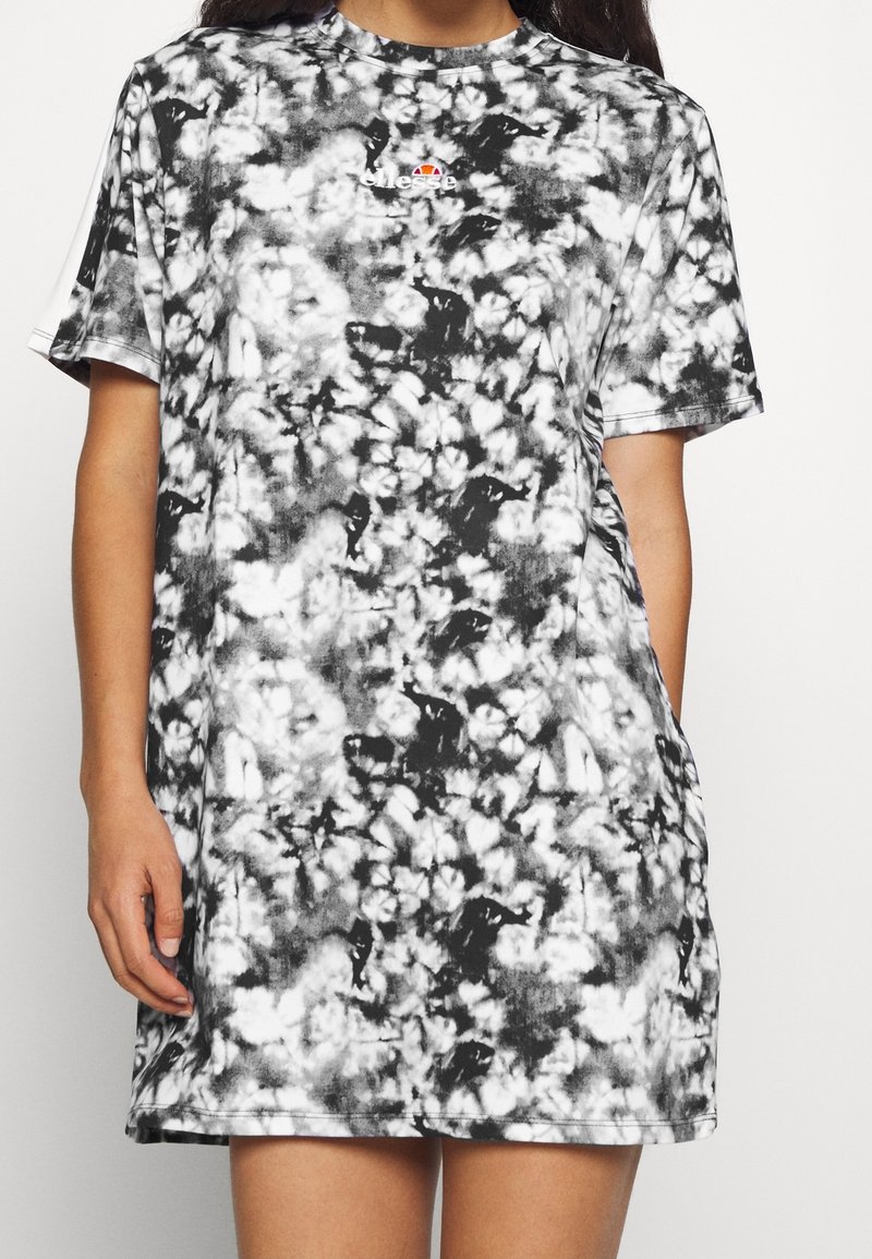 Femme portant une robe T-shirt tie-dye noir et blanc à manches courtes avec un petit logo coloré Ellesse sur la poitrine.