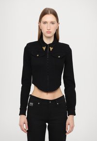 Black cropped jacket with long sleeves, two front pockets, and gold hardware accents on the collar. Smooth texture, button-up front closure.