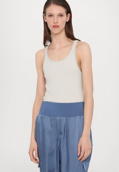 Lichtgrijze geribbelde tanktop met een ronde hals, gedragen met losse blauwe satijnen broek met een elastische tailleband en zijzakken.