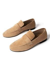 Beige loafers i ruskind med en lav sort hæl, rundet tå og en bred rem over overdelen, vist side om side på en hvid baggrund.