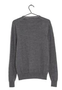 Grauer Strickpullover mit langen Ärmeln und rundem Ausschnitt, der eine glatte Textur sowie gerippte Bündchen und Saum aufweist, hängt an einem schwarzen Haken.