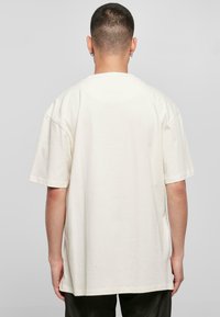 Unisex didelis T-palaidinė off-white medvilnės. Trumpomis rankovėmis, apvaliu kaklu ir laisvu siluetu. Lygus paviršius, be matomų raštų ar detalių.