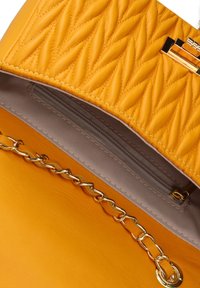 Borsa a tracolla gialla trapuntata con una texture liscia, tracolla in catena dorata e una tasca interna grigia con zip. La chiusura presenta un accento in metallo.