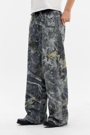 Pantalons larges à imprimé camouflage dans des teintes de gris et de vert, avec une finition texturée et des poches latérales, associés à des chaussures noires.