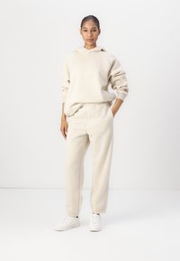 Beige Baumwollkapuzenpullover mit einer Kängurutasche und gerippten Bündchen, kombiniert mit passenden, schmal zulaufenden Jogginghosen mit elastischem Bund und Bündchen.